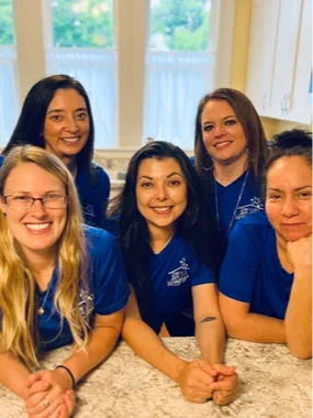 Warm and compassionate cleaning team interaction – Joyful, caring smiles, two cleaners shaking hands with homeowner in a welcoming foyer, tidy surroundings, earth tones, sunbeams, lifelike shadows. Reliable cleaning service human touch